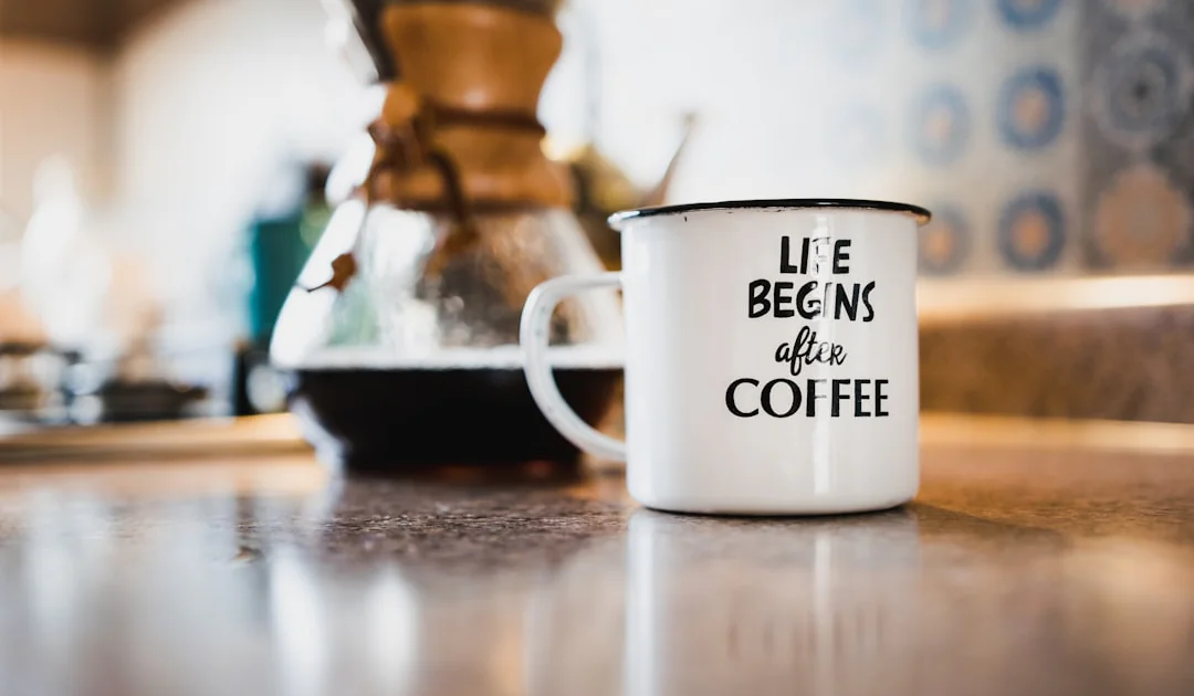 white and black life begins after coffee printed enamel cup beside 1/4 black liquid-filled glass flask on brown wooden panel