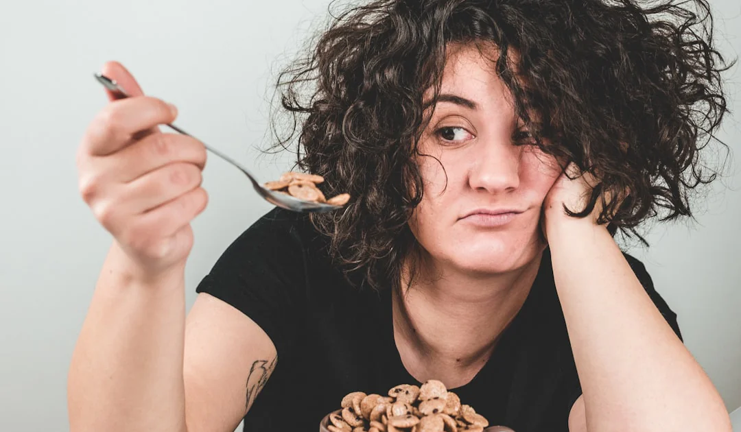 woman with messy hair wearing black crew-neck t-shirt holding spoon with cereals on top
